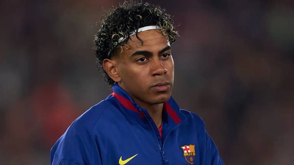 لامين يامال لاعب برشلونة الشاب يرتدي قميص الفريق ويمسك كرة القدم على أرض الملعب.