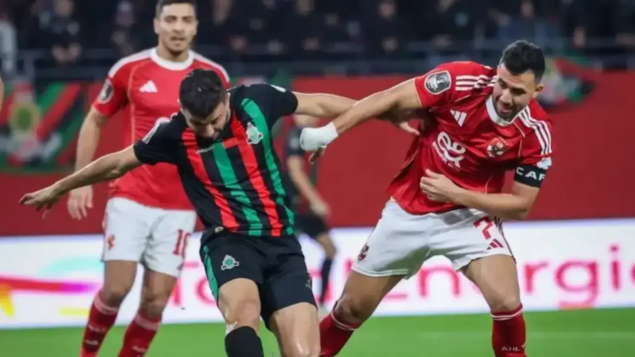 لاعب كرة قدم يرتدي قميصًا مخططًا بالأسود والأخضر في منافسة على الكرة مع لاعبين يرتدون قمصانًا حمراء.