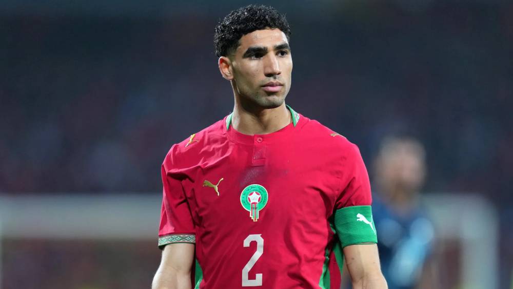 أشرف حكيمي يرتدي قميص المغرب مع رقم 2 ويشير بيده في مباراة المغرب ضد البرازيل.