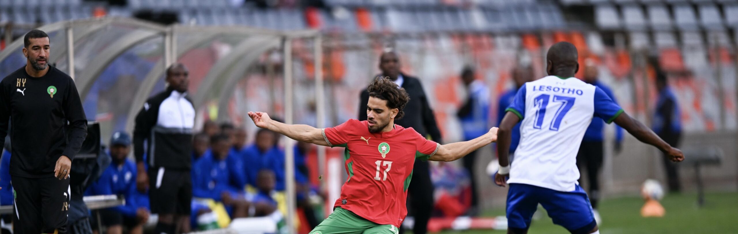 المنتخب الوطني، لاعب يحمل رقم 17 يرتدي زي أخضر وأحمر وأبيض وخصمه يرتدي أزرق وأبيض وبرتقالي.